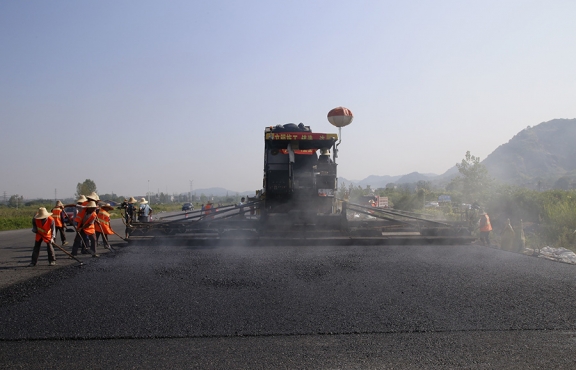 2019年8月，宜春經開區(qū)S311路面攤鋪現場，工友們輔助路面兩側的分料、補窩等作業(yè)
